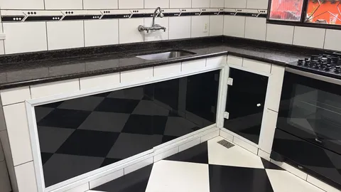 Fechamento sob a pia com vidros escuros e perfis brancos em cozinha com bancada limpa e piso xadrez.