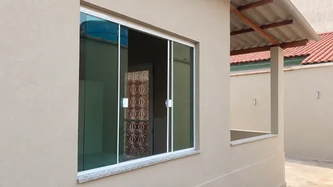 Janela de correr em vidro verde, com puxadores brancos e peitoril de pedra, em parede bege clara.