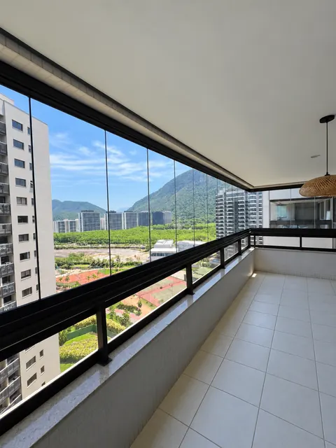 Varanda limpa com fechamento de vidro transparente, perfis pretos e vista para montanhas e prédios.