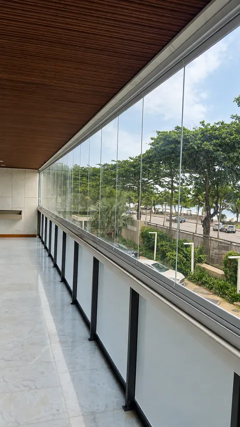 Fechamento de varanda com folhas de vidro transparente e perfis de alumínio, com vista para árvores e rua.